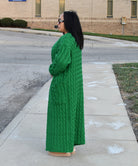 Woman in a green dress standing on a sidewalk with a building in the background