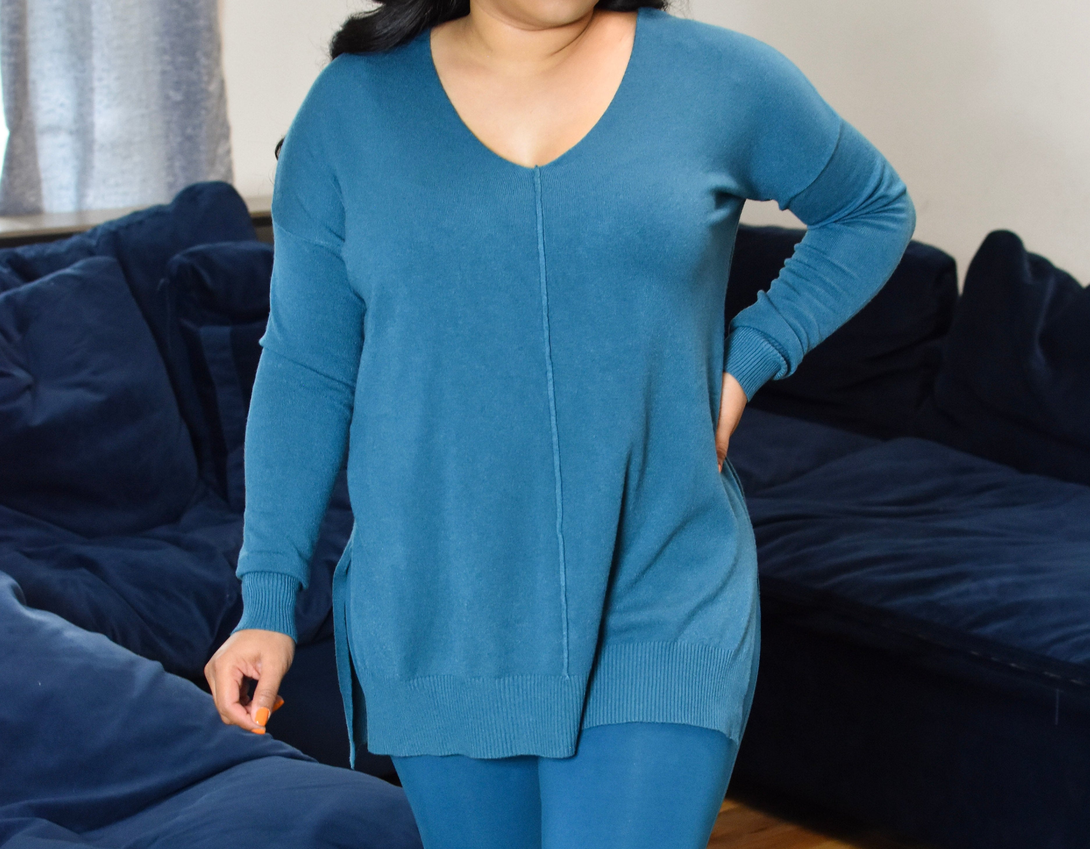 Woman wearing a blue sweater and pants standing in front of a dark blue couch.